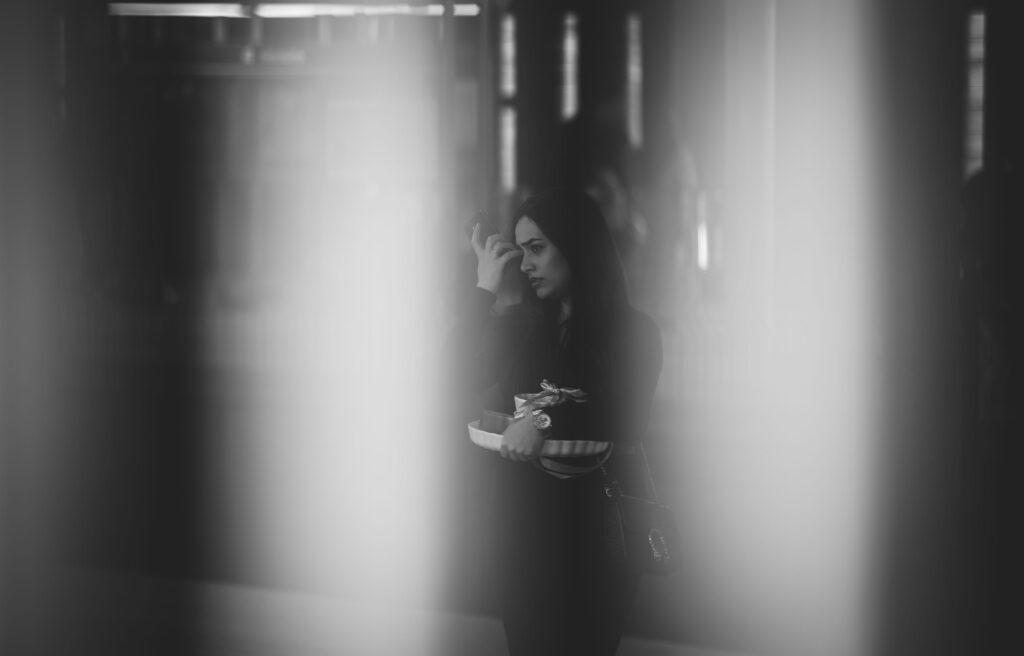 Frau mit Handtasche und Geschenkbox telefoniert in Stockholm, durch unscharfe Lichtstreifen hindurch fotografiert.