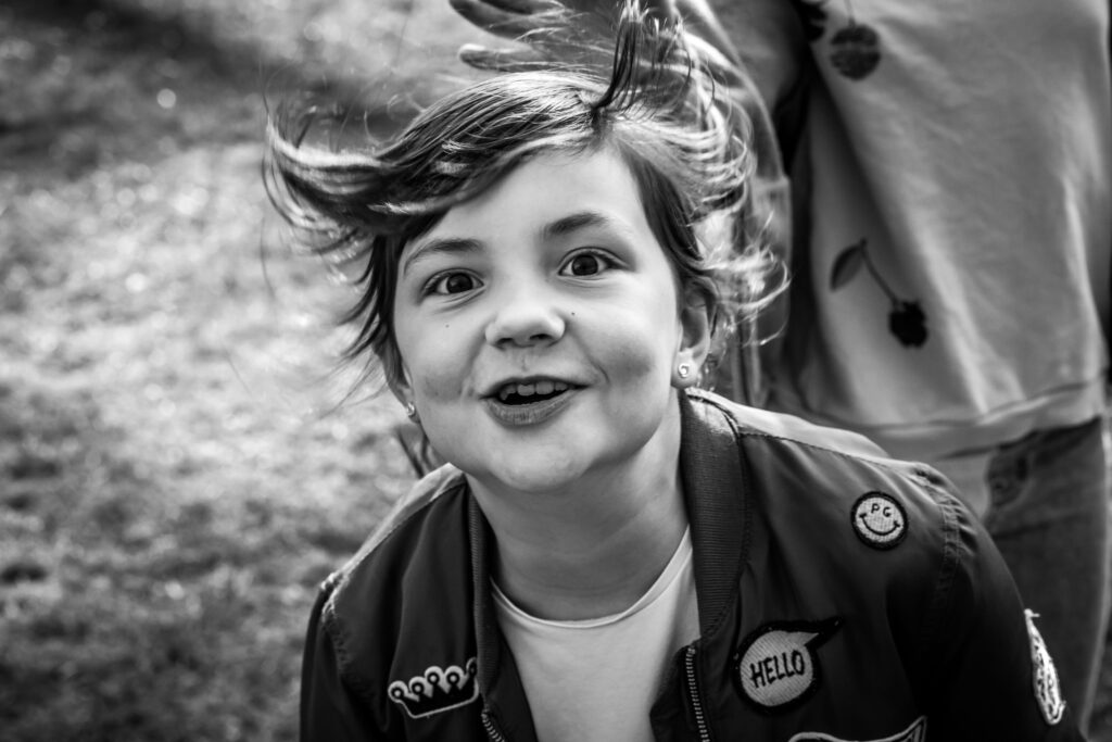 Fröhliches Kind mit flatternden Haaren schaut lachend in die Kamera.