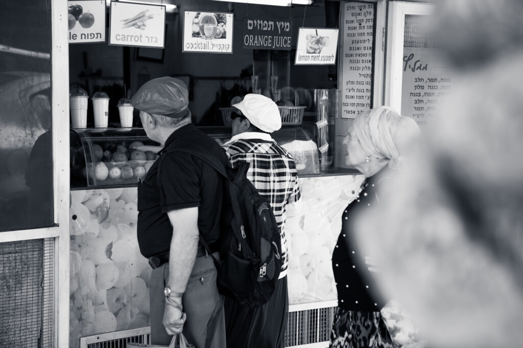Menschen warten vor einem Saftstand mit Schildern für Karottensaft, Orangensaft und Cocktails, Straßenszene in Tel Aviv.
