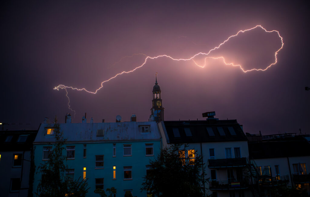Blitz erhellt den Nachthimmel über dem Michel und Wohnhäusern in Hamburg.
