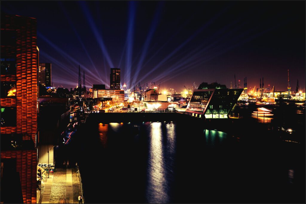 Nachtaufnahme des Hamburger Hafens an der Elbe mit Dockland und Lichtershow über der Skyline am Wasser.