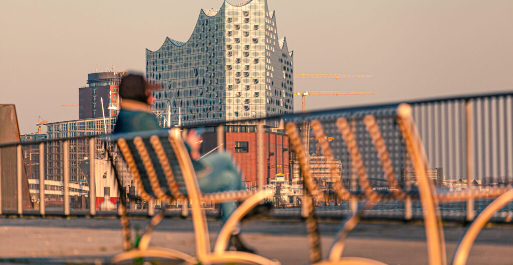 Blick auf die Hamburger Elbphilharmonie bei Sonnenuntergang, unscharfe Person auf einer Bank im Vordergrund.