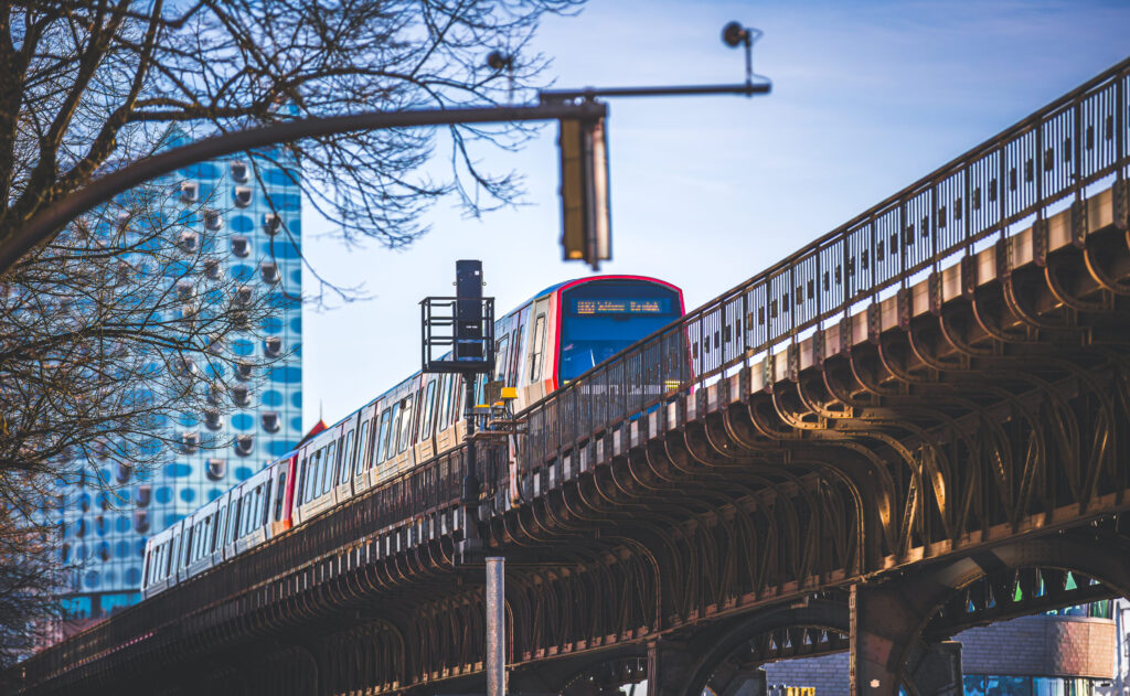 U-Bahn fährt auf Hochbahntrasse vor der Elbphilharmonie bei blauem Himmel in Hamburg.