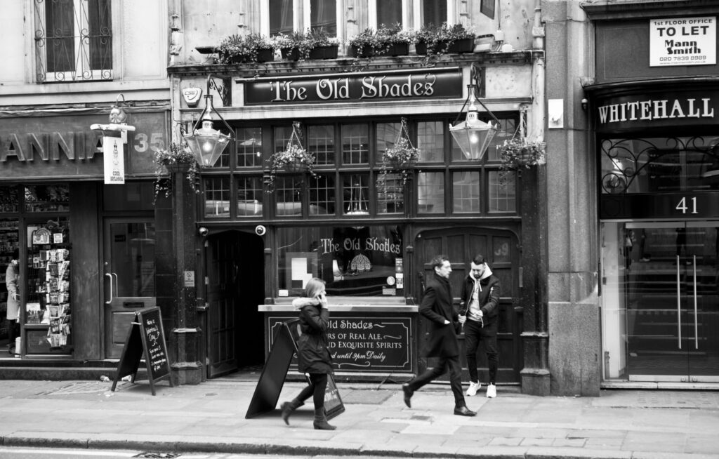 Schwarz-weiß Foto vom Pub The Old Shades in Whitehall London, mit vorbeigehenden Passanten vor der historischen Fassade.