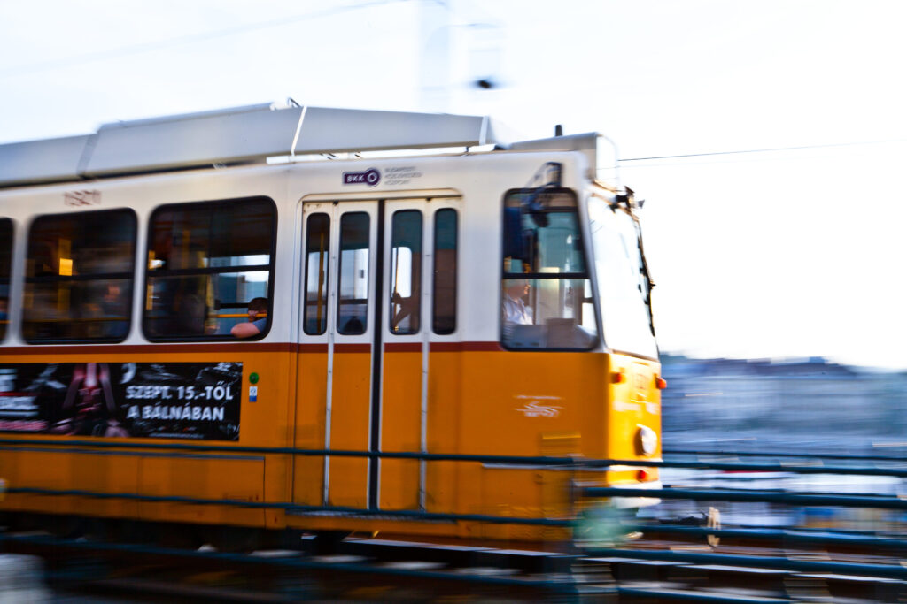 Gelbe Straßenbahn fährt in Bewegung durch Budapest, Passagiere im Inneren, verschwommener Hintergrund.