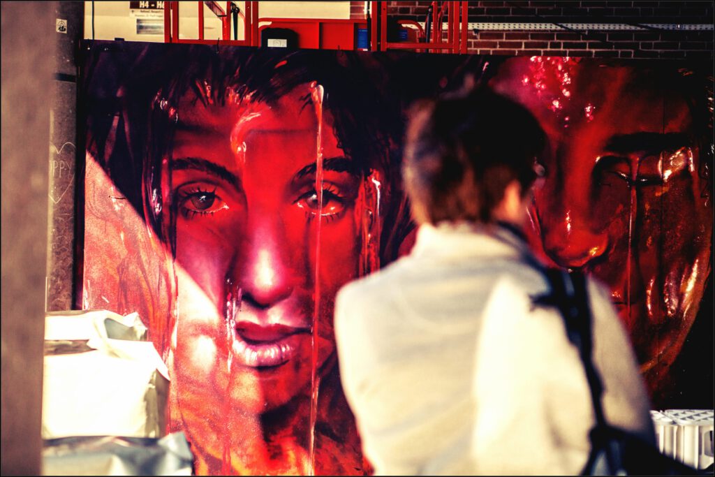 Streetart-Porträt in Rot auf der Millerntor Gallery in Hamburg, betrachtet von einer Dame.