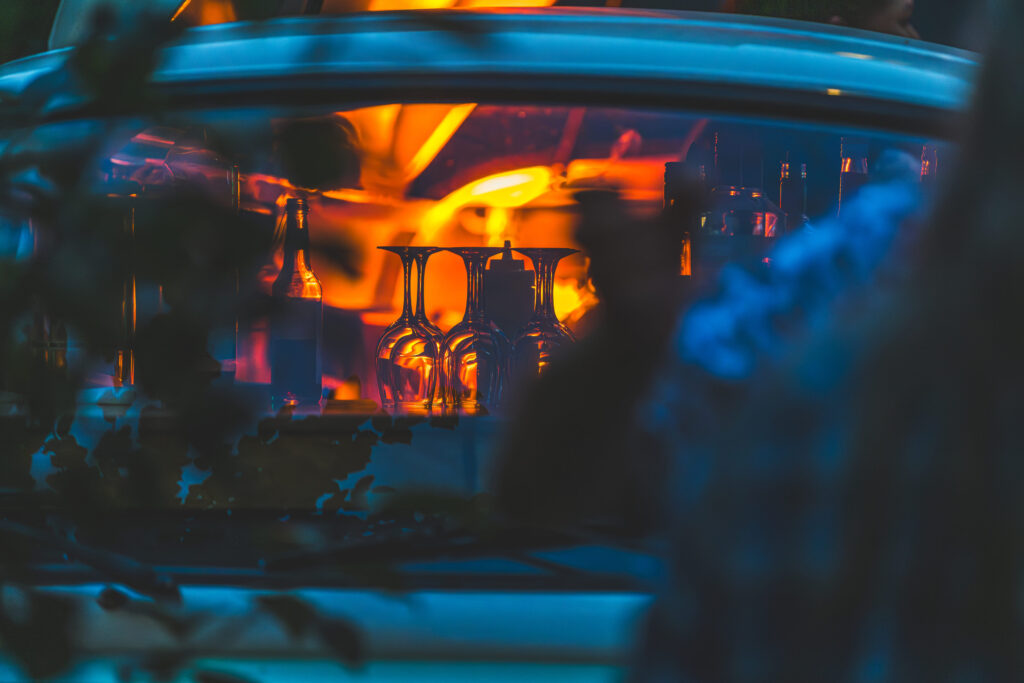 Leuchtende Gläser und Flaschen in einer Bar, warmes orangefarbenes Licht spiegelt sich in der Szene.