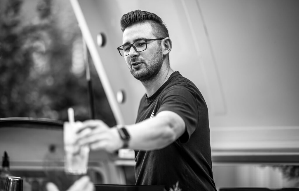 Bartender reicht ein Getränk über den Tresen, Schwarz-Weiß-Aufnahme mit klaren Details.