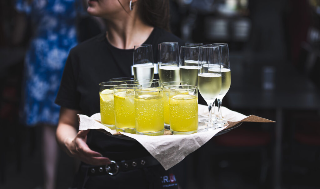 Kellnerin serviert ein Tablett mit gelben Drinks und Sektgläsern beim Empfang.