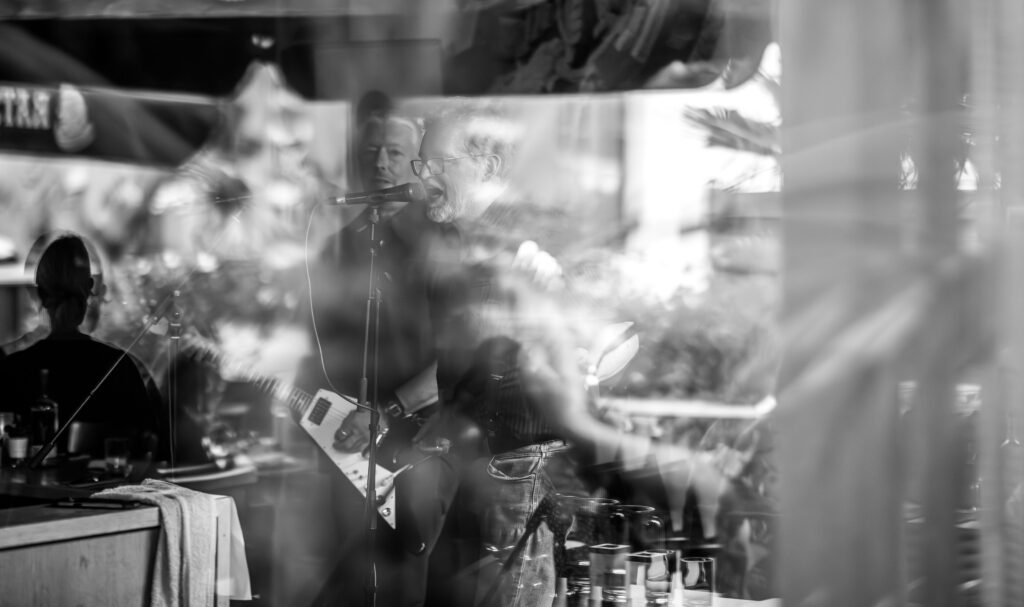 Schwarz-weiß-Foto einer Band mit Gitarren und Gesang, teils durch Spiegelungen verdeckt, Konzert in der Trude Hamburg.