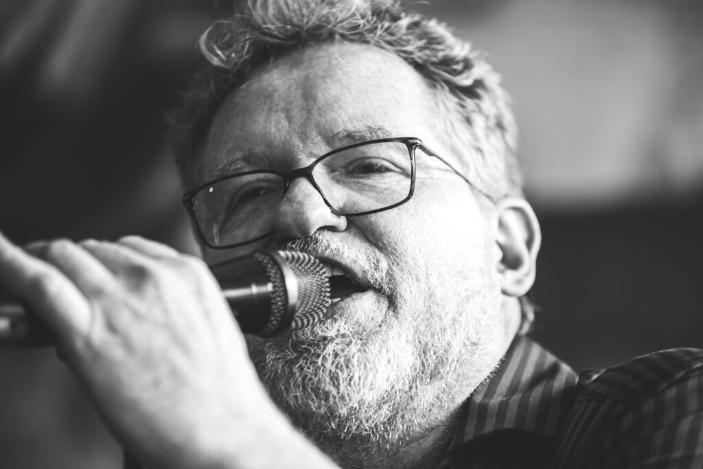 Sänger mit Brille und Bart singt ins Mikrofon, Nahaufnahme in Schwarzweiß.