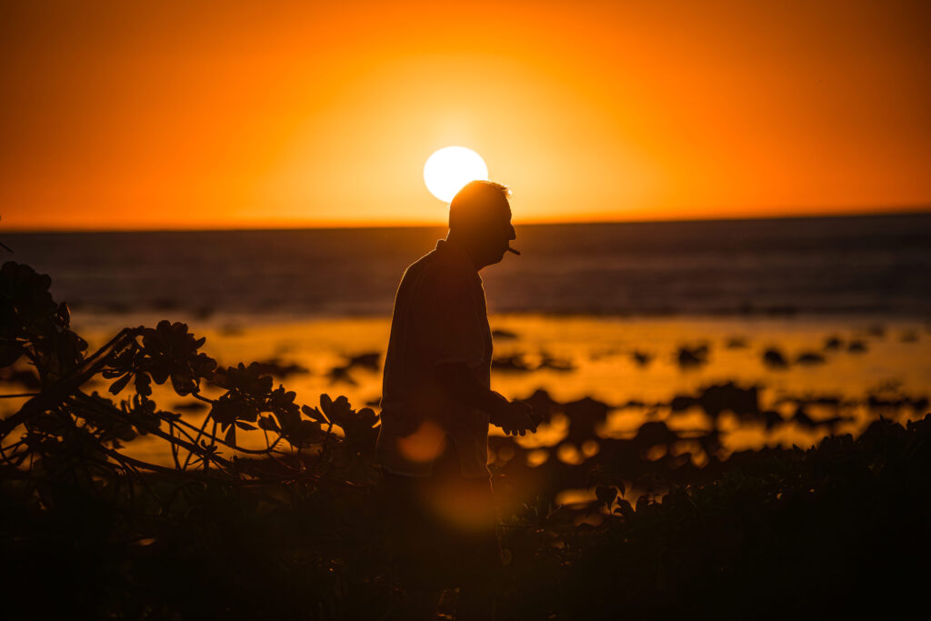 Mauritius Sonnenuntergang: Silhouette eines Mannes mit Zigarre vor orangefarbenem Himmel und Meer.