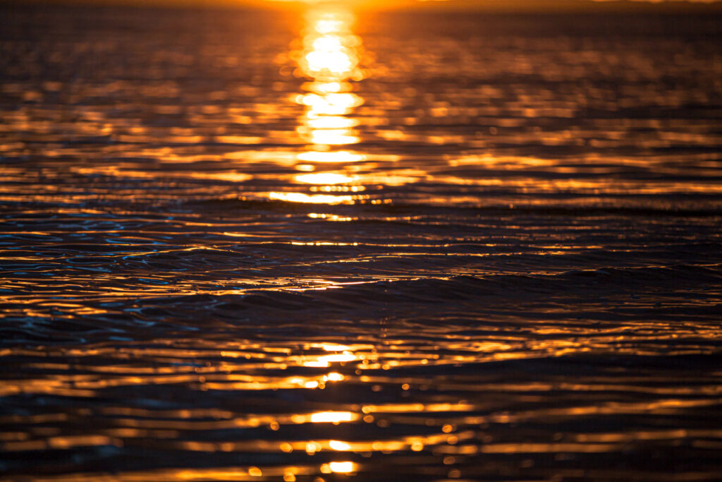 Goldene Lichtreflexe der untergehenden Sonne auf sanften Wellen des Meeres bei Sonnenuntergang.