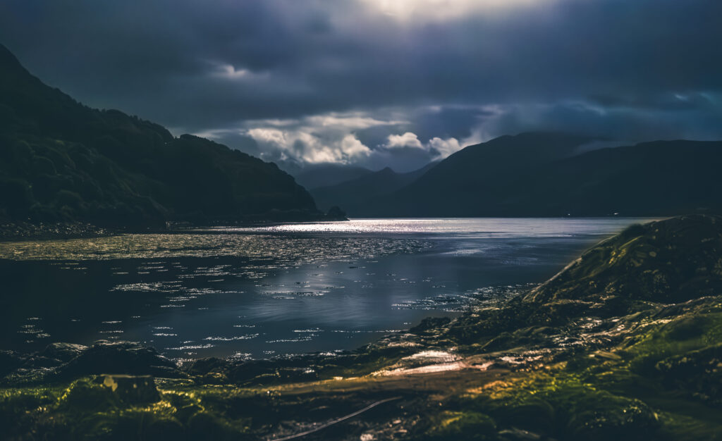 Dramatische Wolken über einem schottischen Loch, Licht spiegelt sich im Wasser.