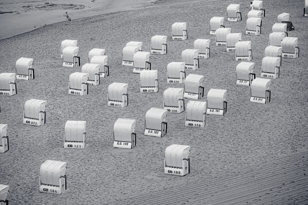 Reihen von nummerierten Strandkörben auf leerem Sandstrand an der Ostseeküste, aufgenommen in Schwarzweiß.