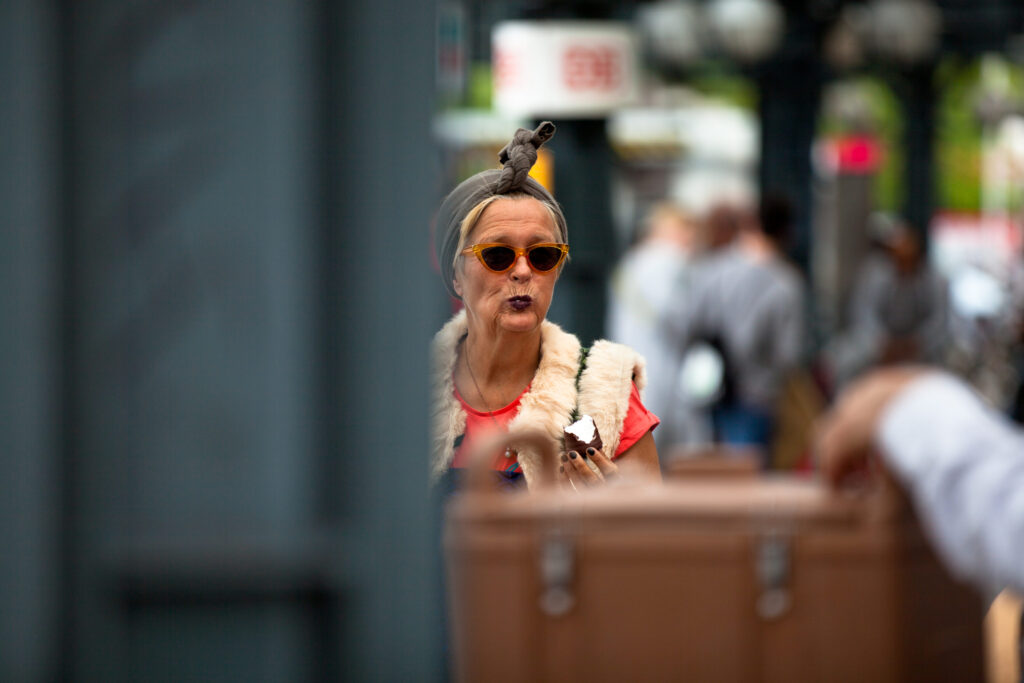Frau mit Sonnenbrille und Kopftuch isst einen Schokokuss am Hamburger Hauptbahnhof.