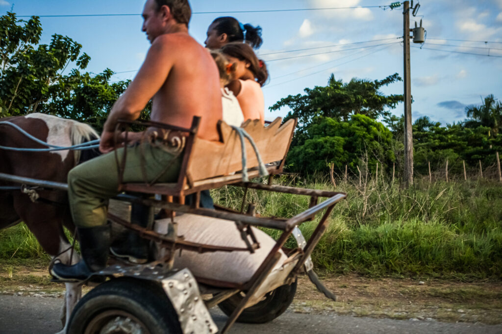 Kubanische Familie fährt mit einer Pferdekutsche durch das Viñales-Tal, ein Sack mit Getreide liegt im Wagen.