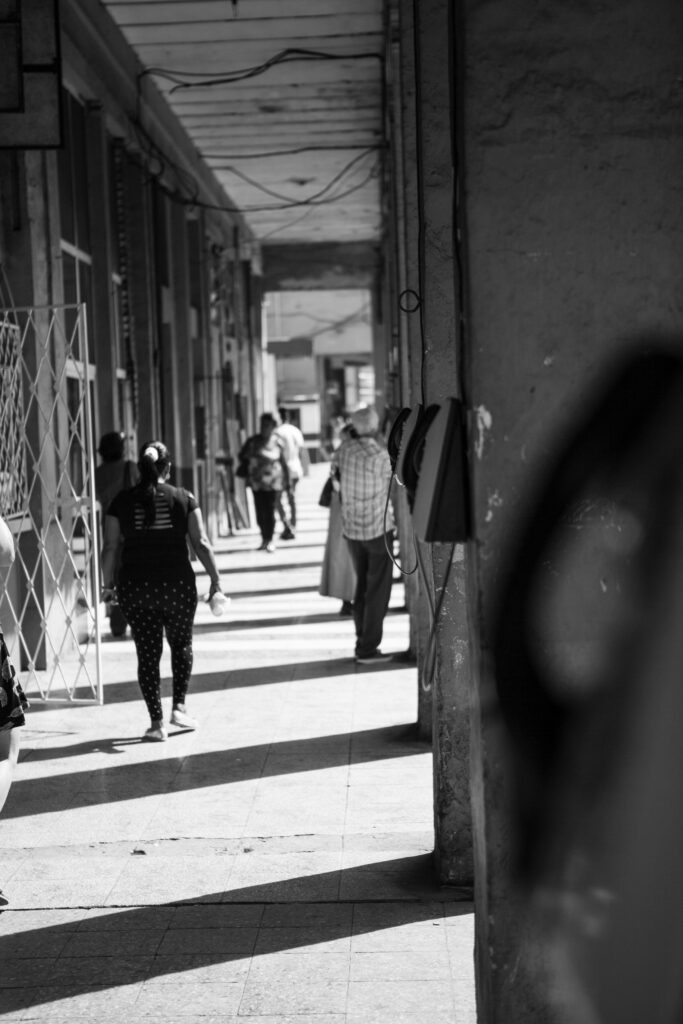 Passanten gehen durch einen überdachten Arkadengang in Havanna, Kuba; alte Telefonhörer hängen an einer Säule im Vordergrund.